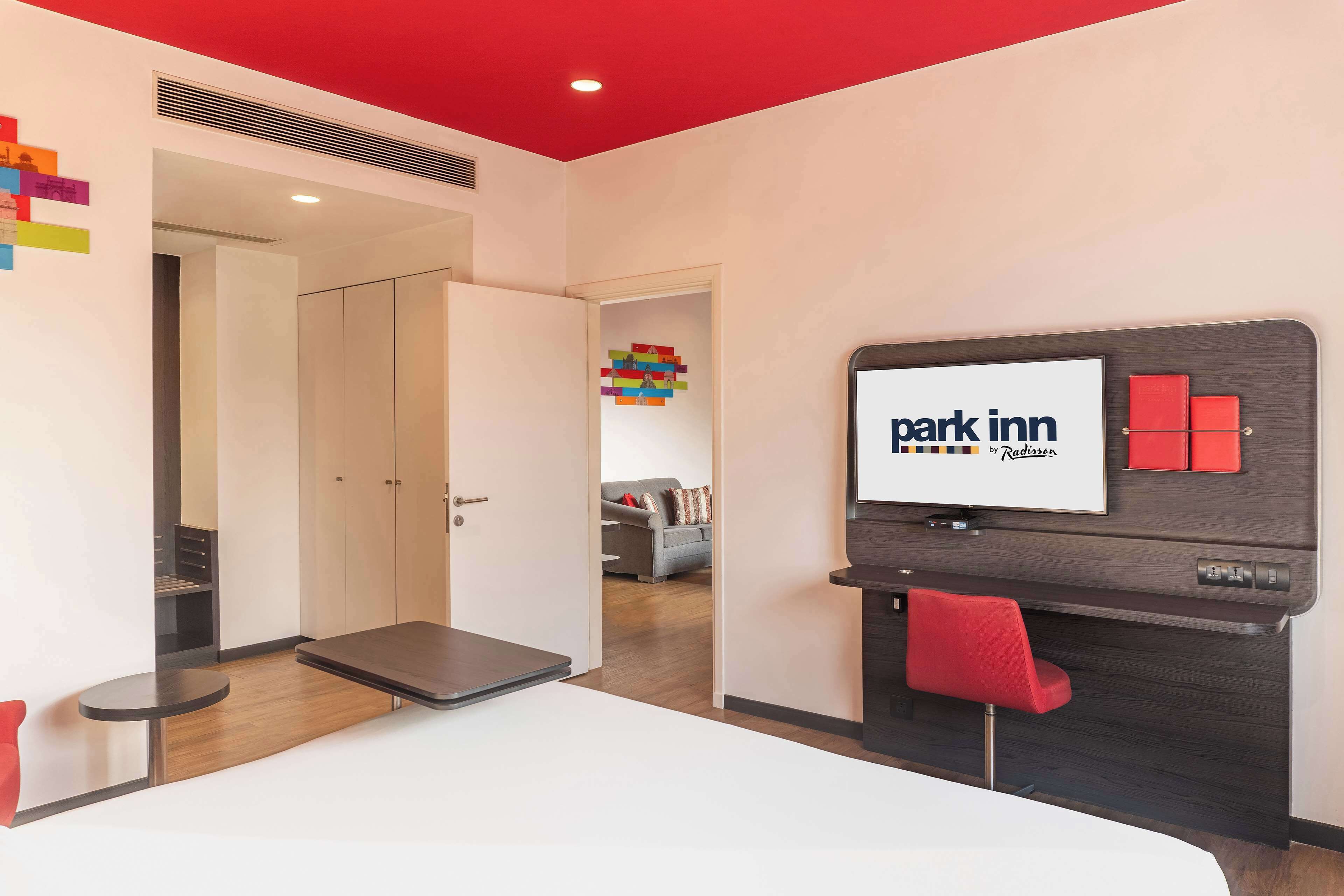A hotel room with a bed, a TV, a desk, and a red chair.
