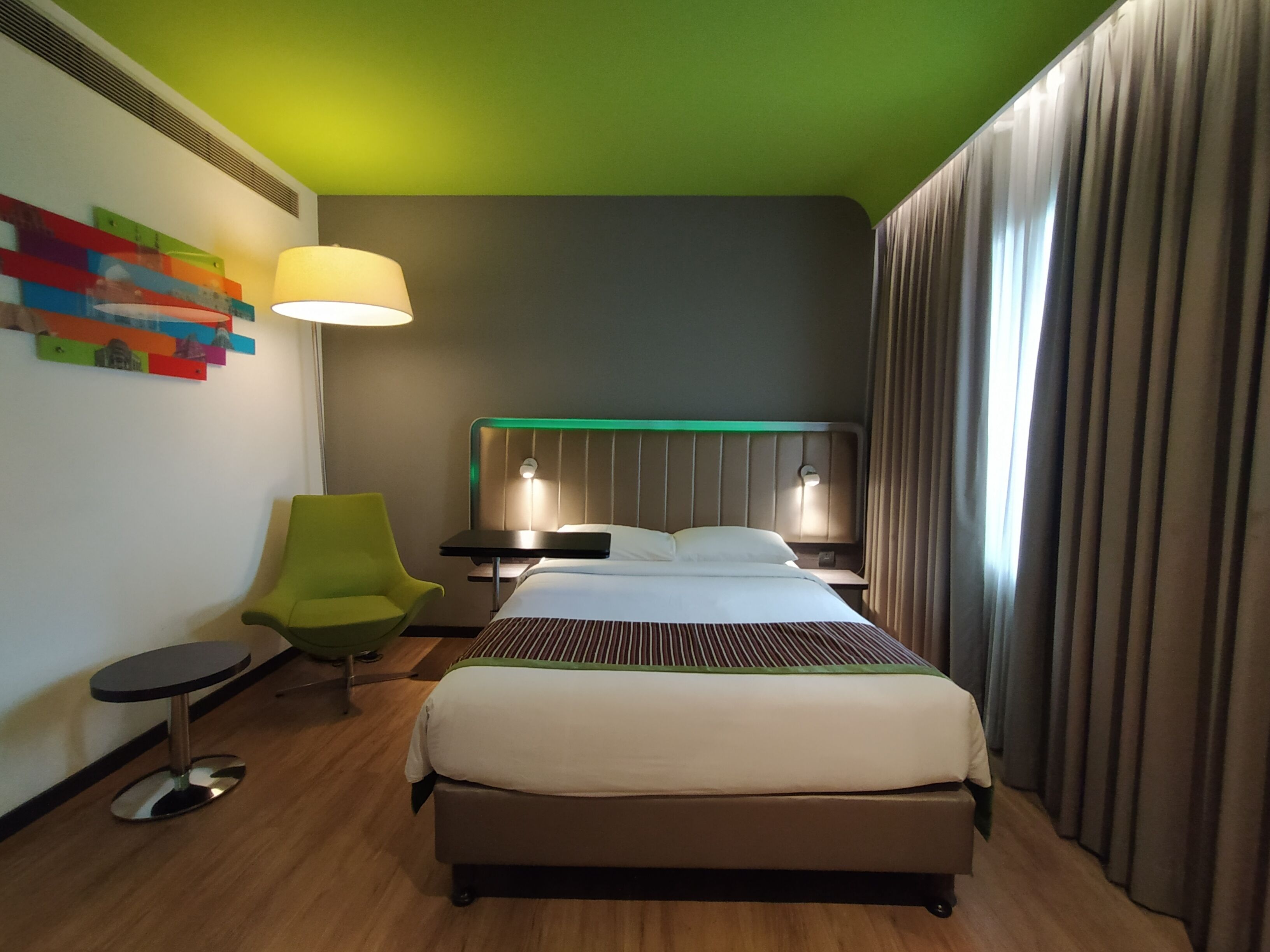 A hotel room with a bed, a chair, a table, and a lamp.