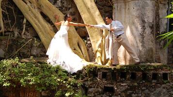 A couple holding hands on a stone platform with a large tree trunk in the background.