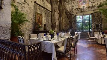 Un restaurante con paredes de piedra, un gran árbol y vistas al verde exterior.