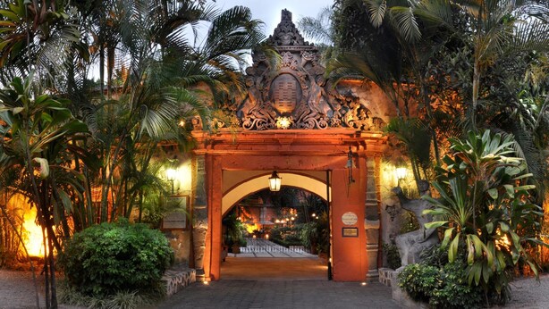 Una entrada ornamentada con un arco central, rodeada de exuberante vegetación tropical e iluminada por una cálida luz.
