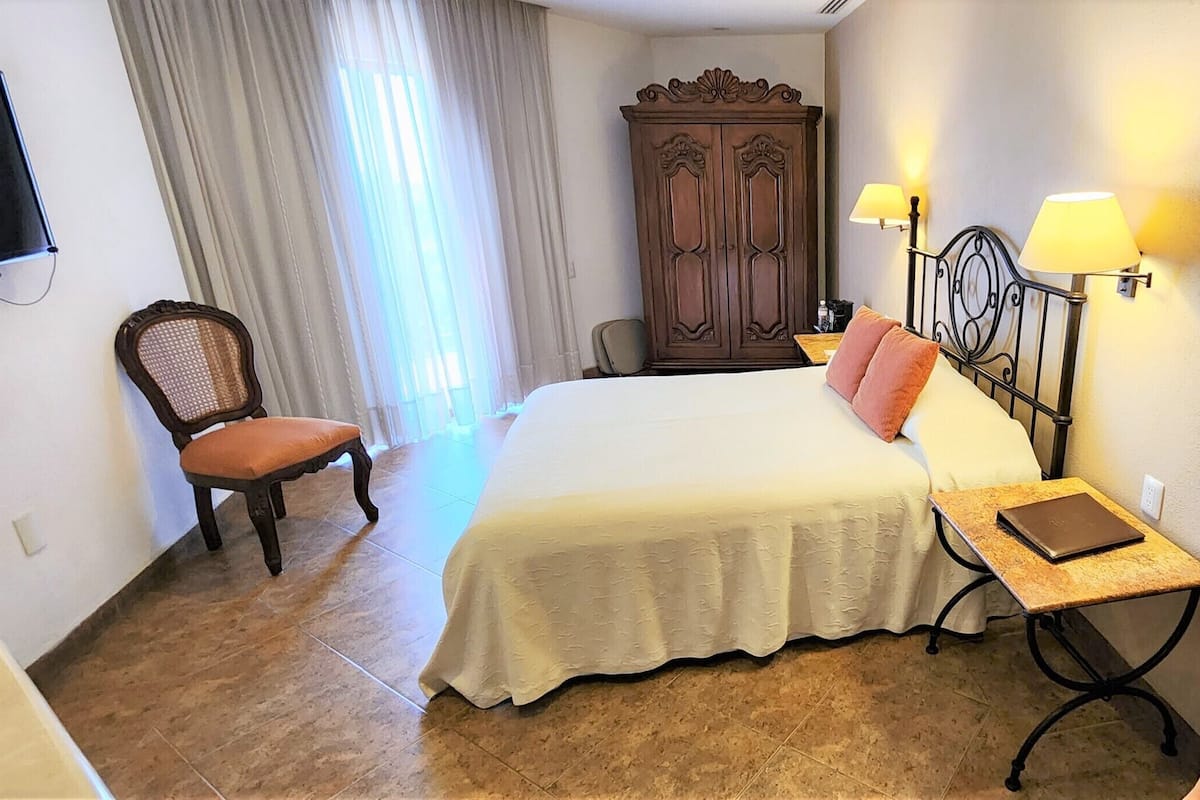 Ein Hotelzimmer mit einem Bett, einem Holzschrank, einem Schreibtisch mit einem Laptop, einem Sessel und einem Fernseher an der Wand.