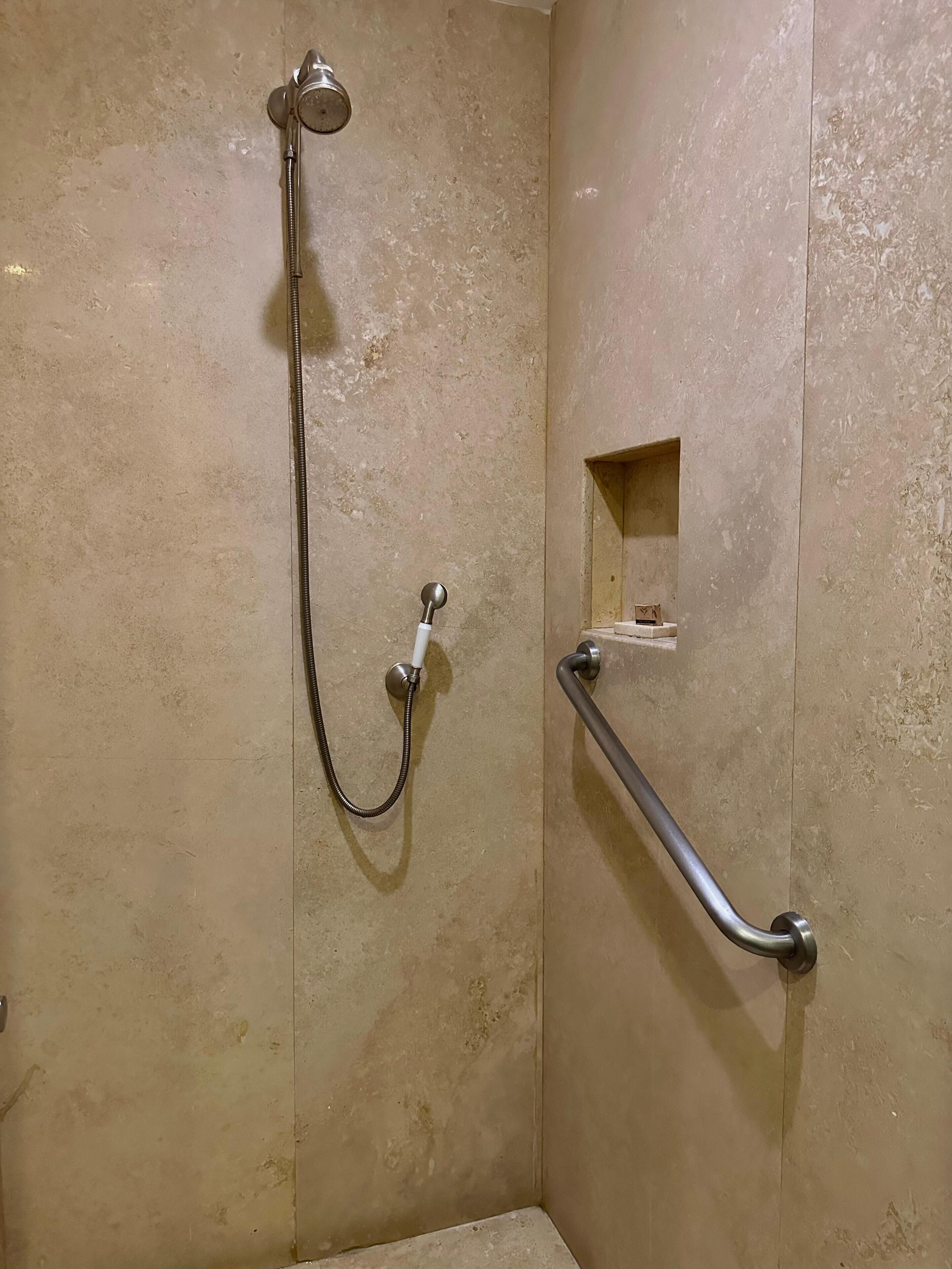 Zona de ducha con cabezal de ducha de mano y barra de apoyo.