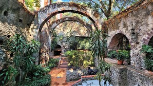 Un jardín interior con arcos de piedra, plantas en macetas y un sendero.