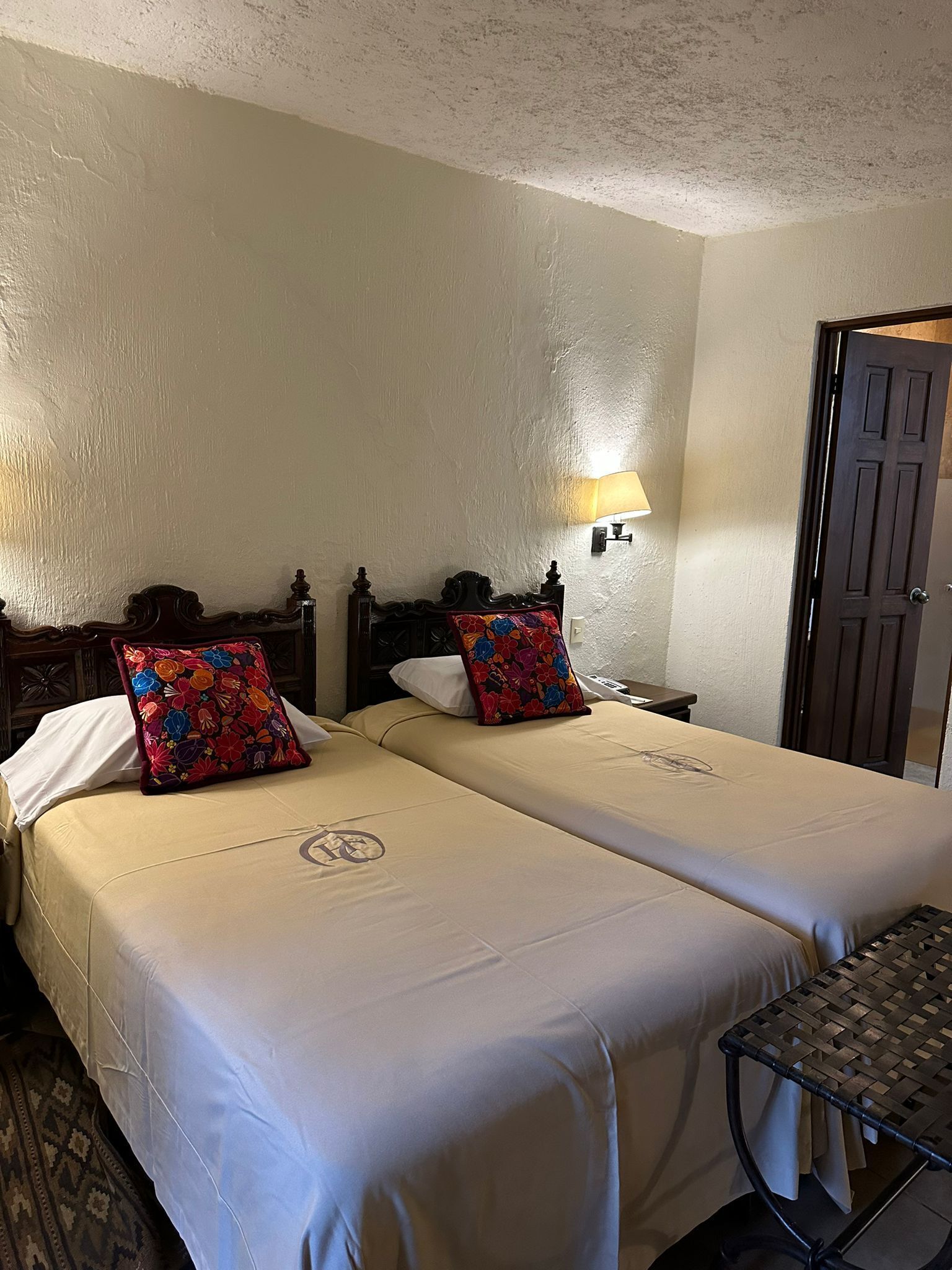 A hotel room with two beds, a nightstand, a lamp, and a door.