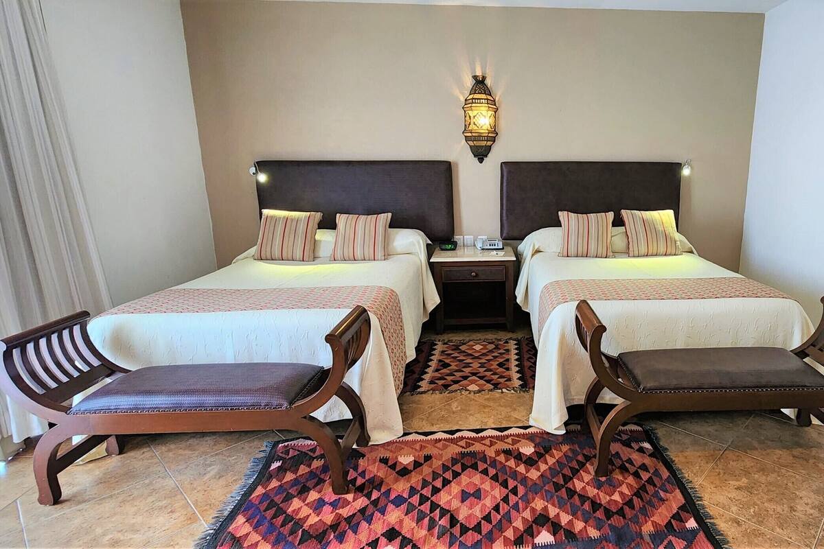 Ein Hotelzimmer mit zwei Betten, Nachttischen, einem Teppich und einem gerahmten Bild an der Wand.
