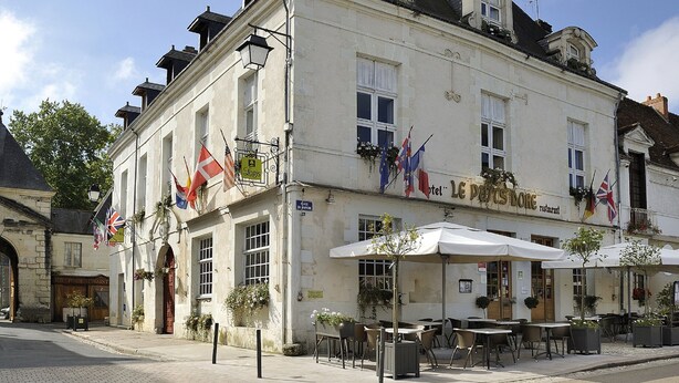 A historic building with multiple flags, outdoor seating, and a sign indicating a restaurant. - Le Puits Doré – Hôtel Restaurant Logis (Richelieu)
