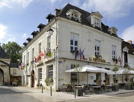 Un bâtiment historique orné de plusieurs drapeaux, doté d’une terrasse et d’une enseigne indiquant qu’il s’agit d’un restaurant.