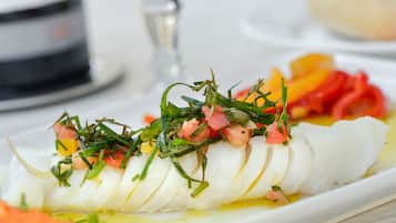 A white plate with sliced white fish topped with green herbs and diced tomatoes.
