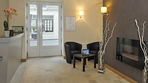 A reception area with a reception desk, two chairs, a wall-mounted TV, a fireplace, and a door leading outside. - Le Puits Doré – Hôtel Restaurant Logis (Richelieu)