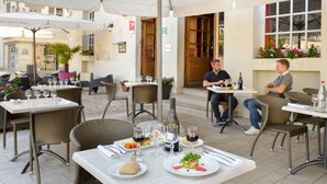 An outdoor cafe with tables and chairs, wine glasses, and bottles. - Le Puits Doré – Hôtel Restaurant Logis (Richelieu)