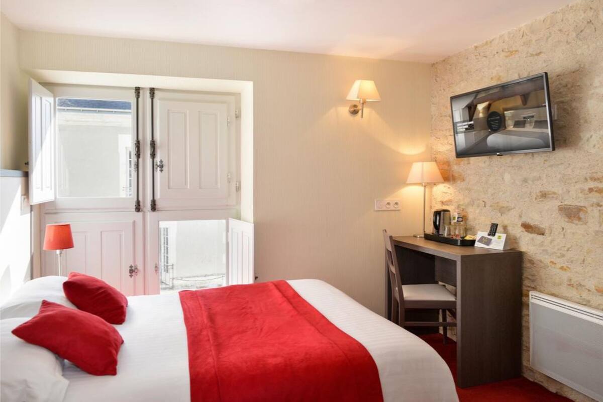 Una habitación de hotel con cama, escritorio, silla, televisión y puerta.