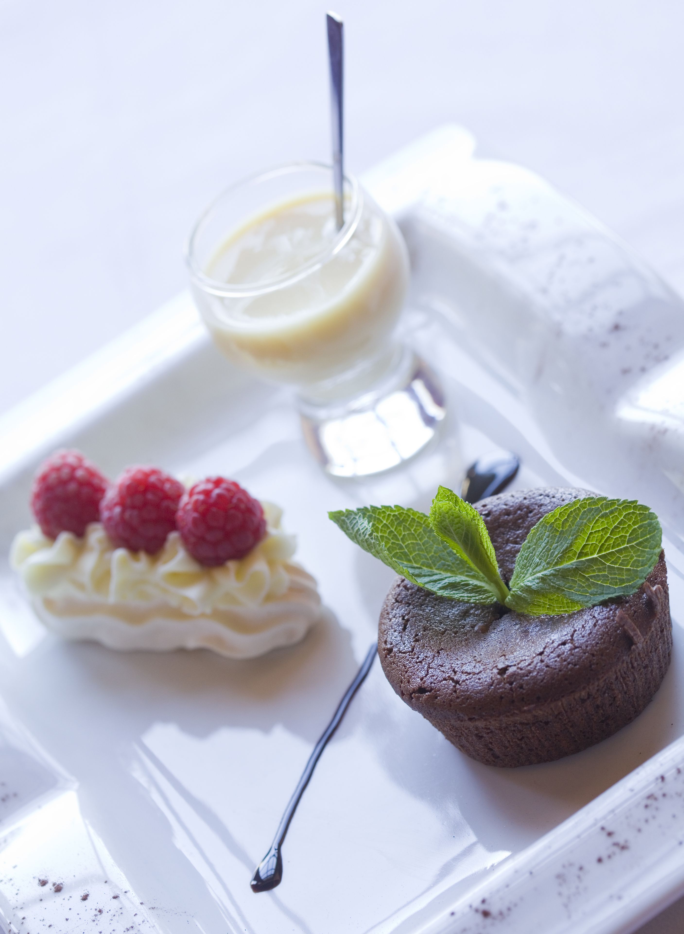 Ett fat med efterrätter innehållande en chokladkaka, en grädddessert med hallon och ett litet glas grädde.