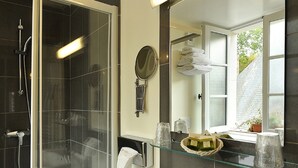 A bathroom with a glass shower enclosure, a white sink, a mirror, and a window with a view of greenery outside. - Le Puits Doré – Hôtel Restaurant Logis (Richelieu)