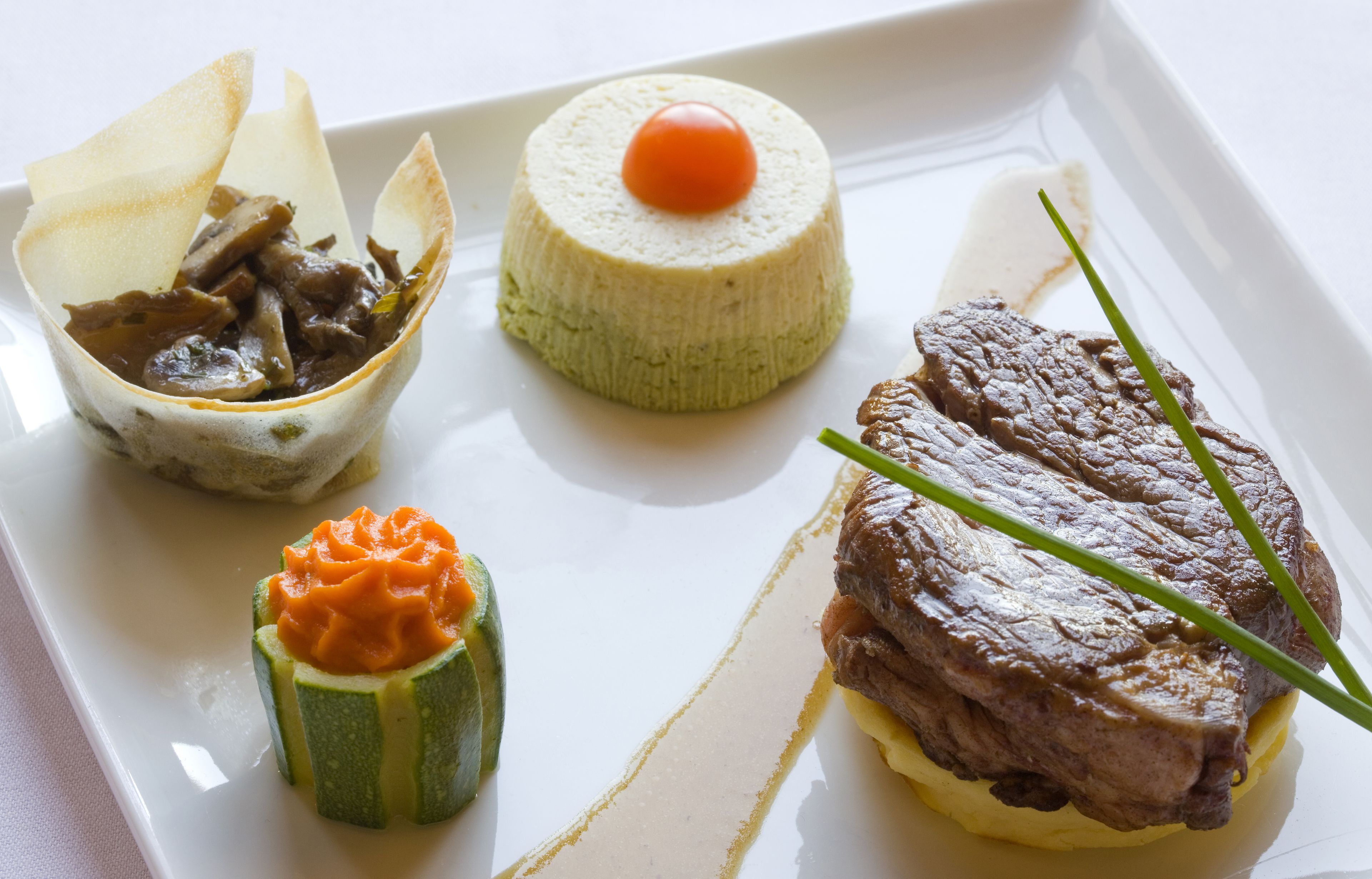A plate with a beef steak, a round cheese with a cherry, and a vegetable dish.