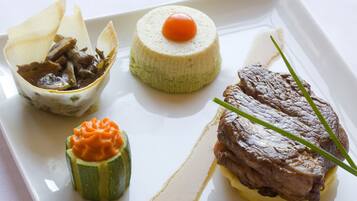 A plate with a beef steak, a round cheese with a cherry, and a vegetable dish.