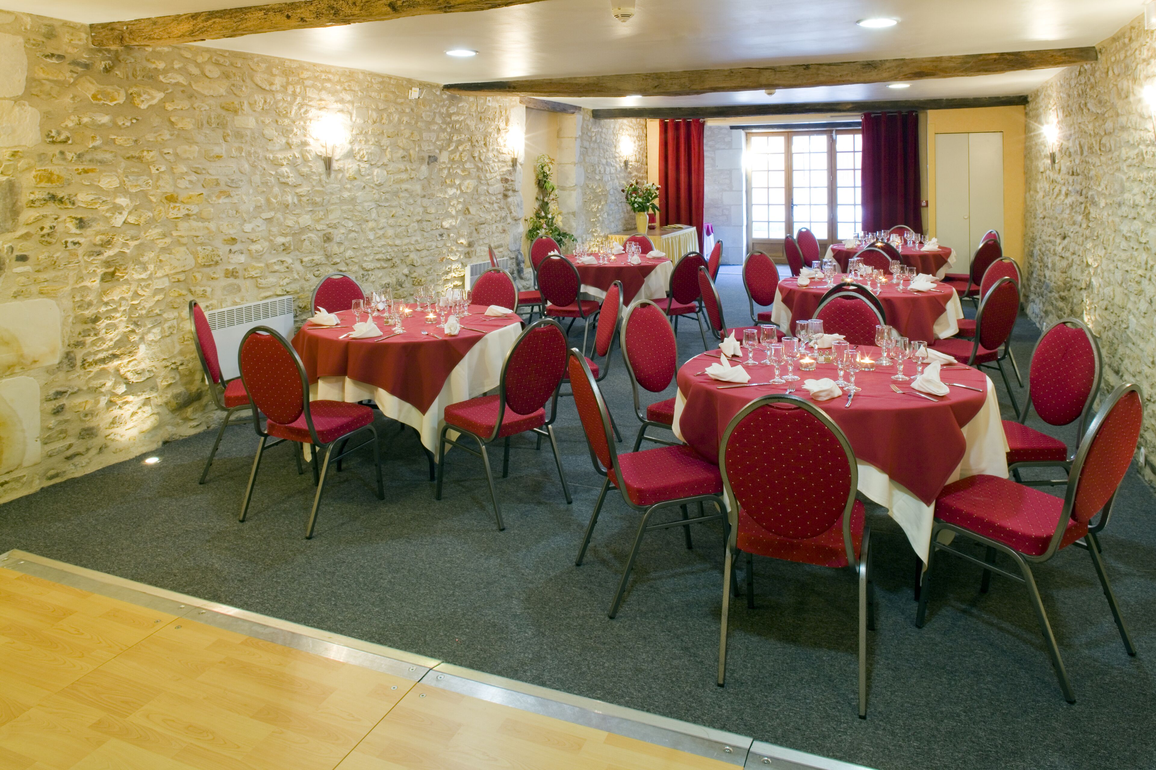 A dining area with stone walls, red tables, and matching chairs.
