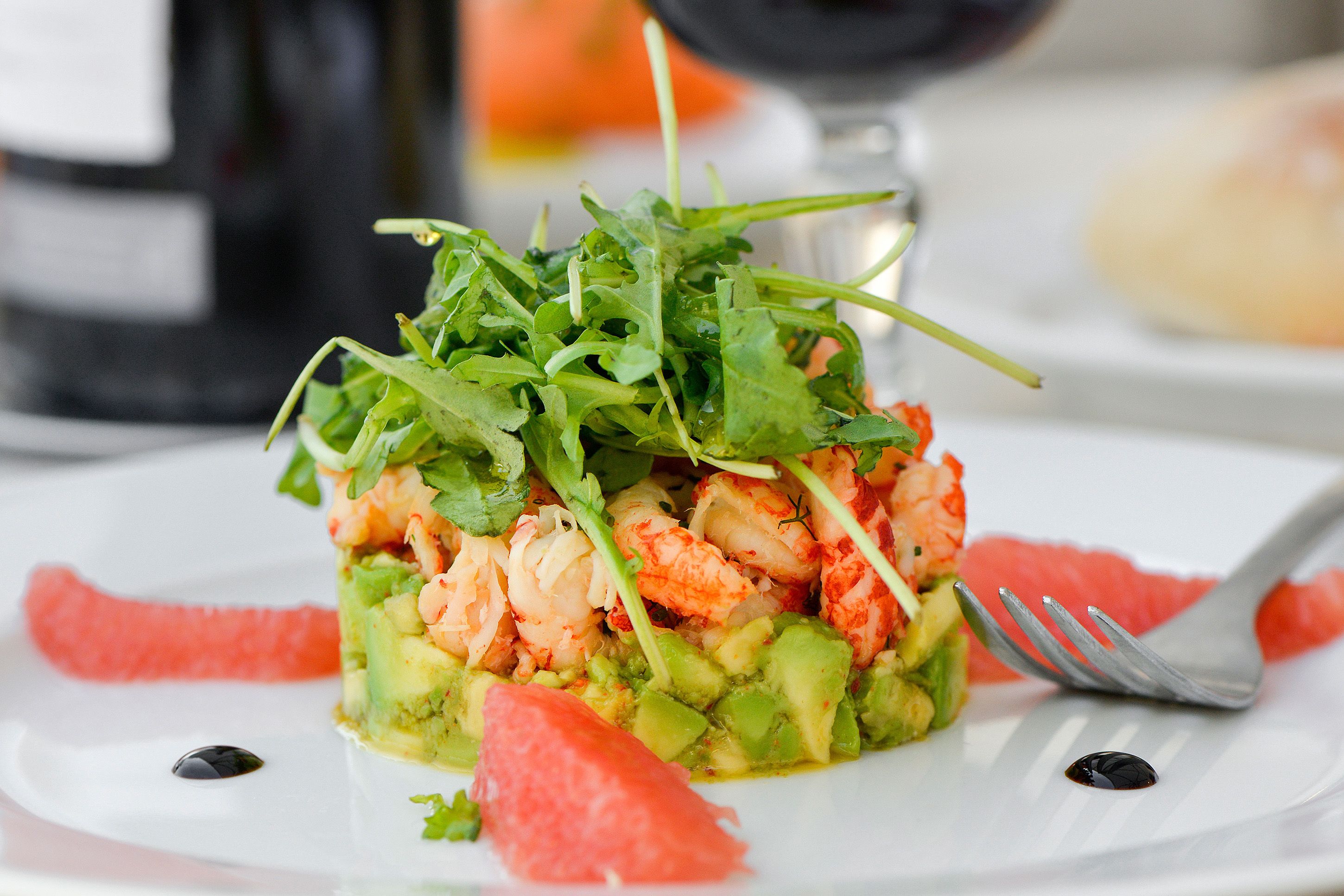 A seafood dish with avocado and greens on a white plate.