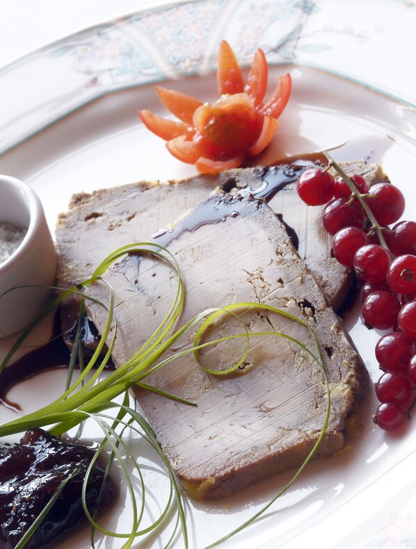 A plate with sliced meat, red currants, and a decorative carrot.