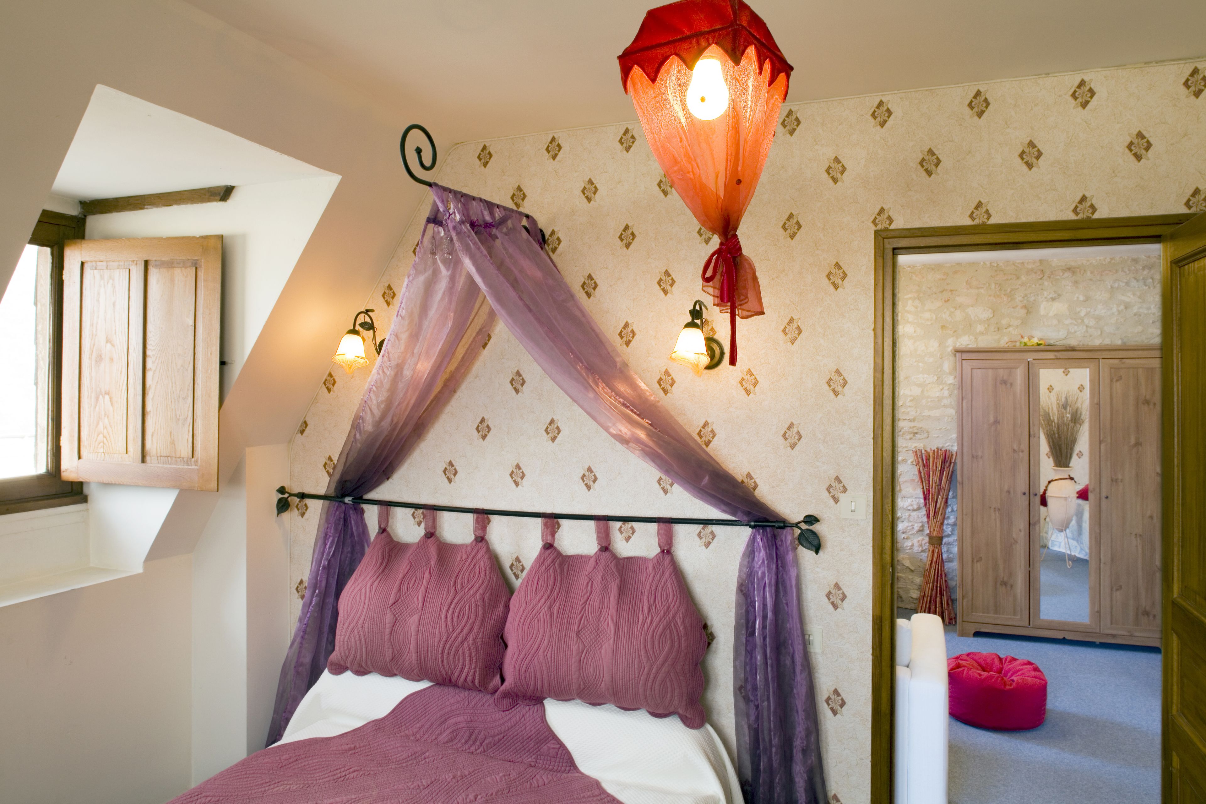 Un dormitorio con cama con dosel, un armario de madera y un farol decorativo.