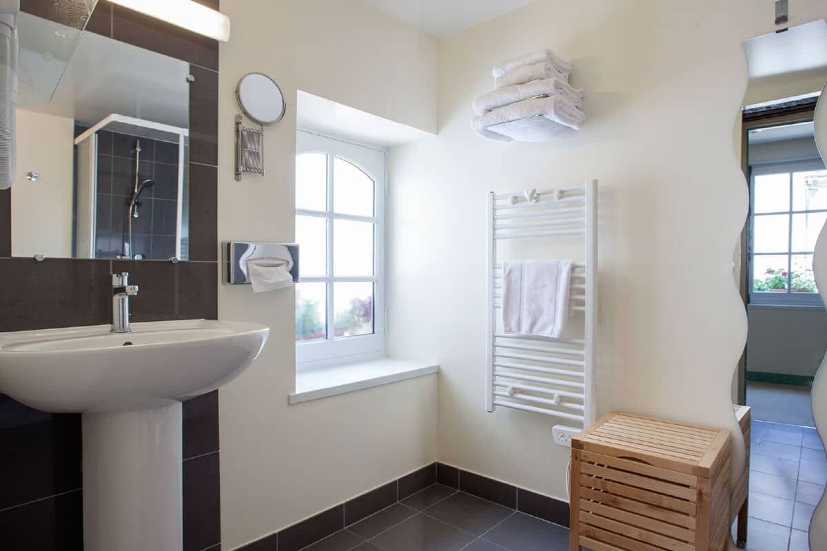 A bathroom with a sink, mirror, window, towel rack, and a wooden stool.