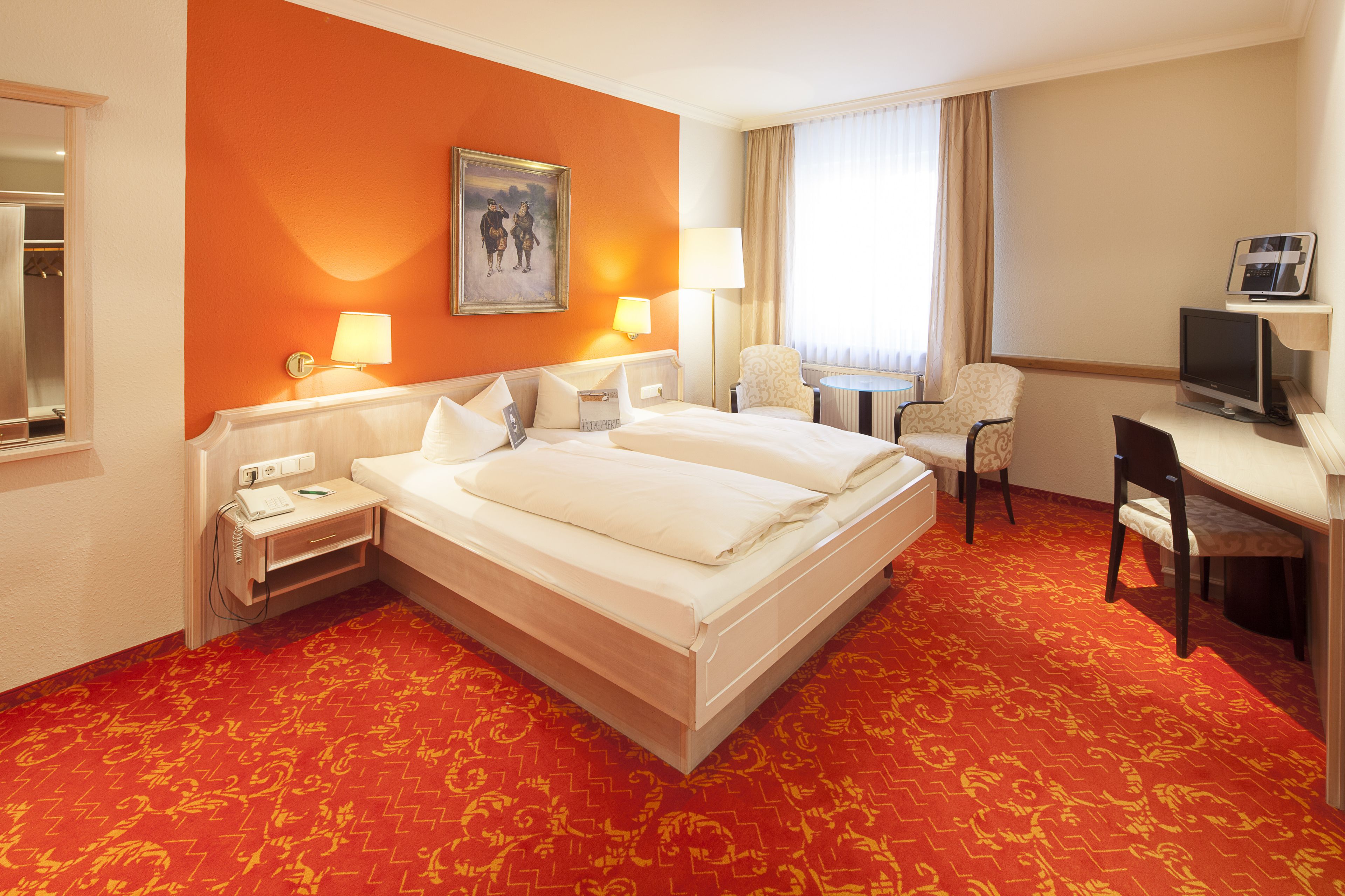 A hotel room with a large bed, two bedside tables, a desk with a chair, a television, and a window with curtains.