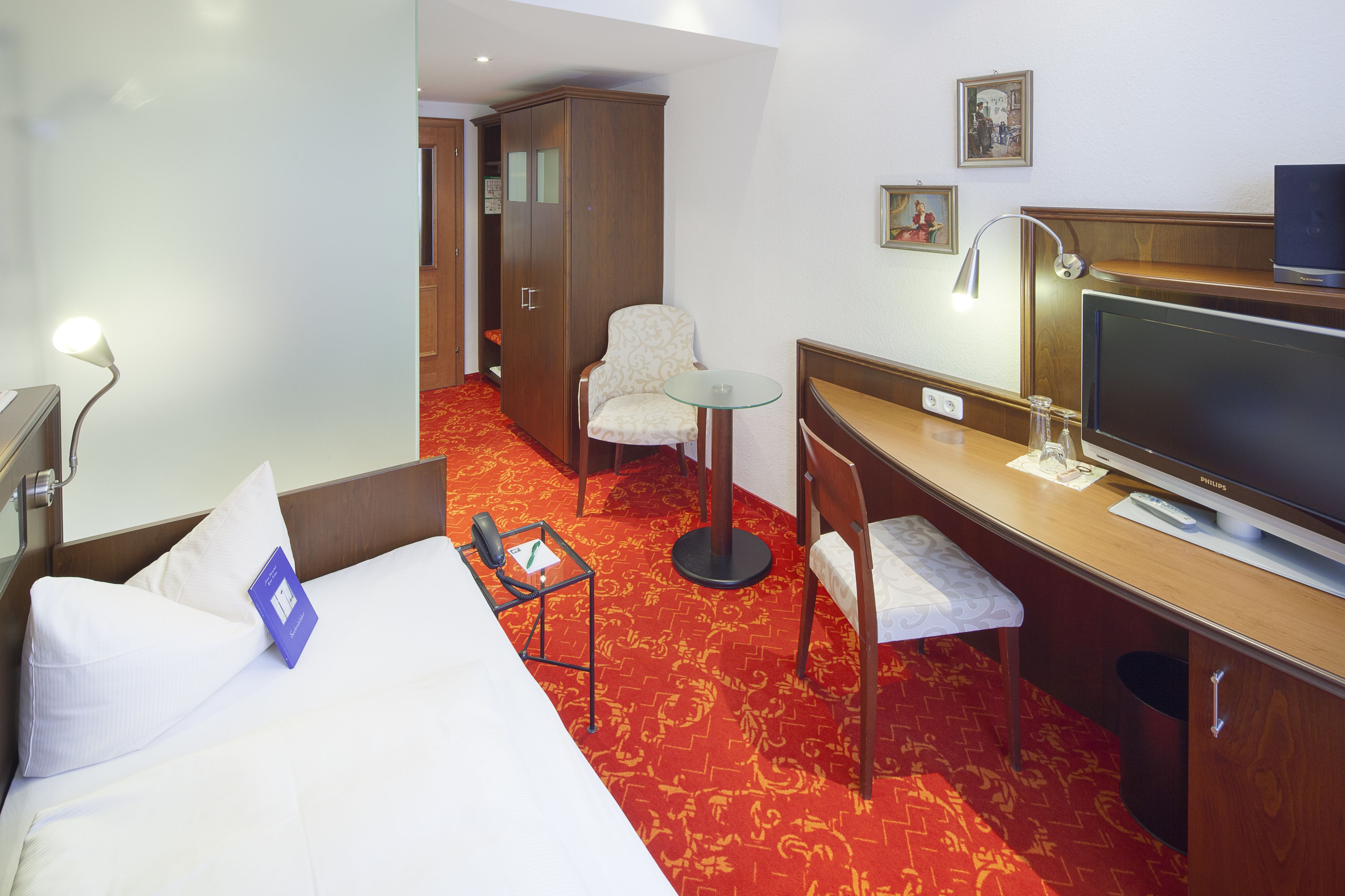 Ett hotellrum med en säng, ett skrivbord, en stol, en tv och en garderob.