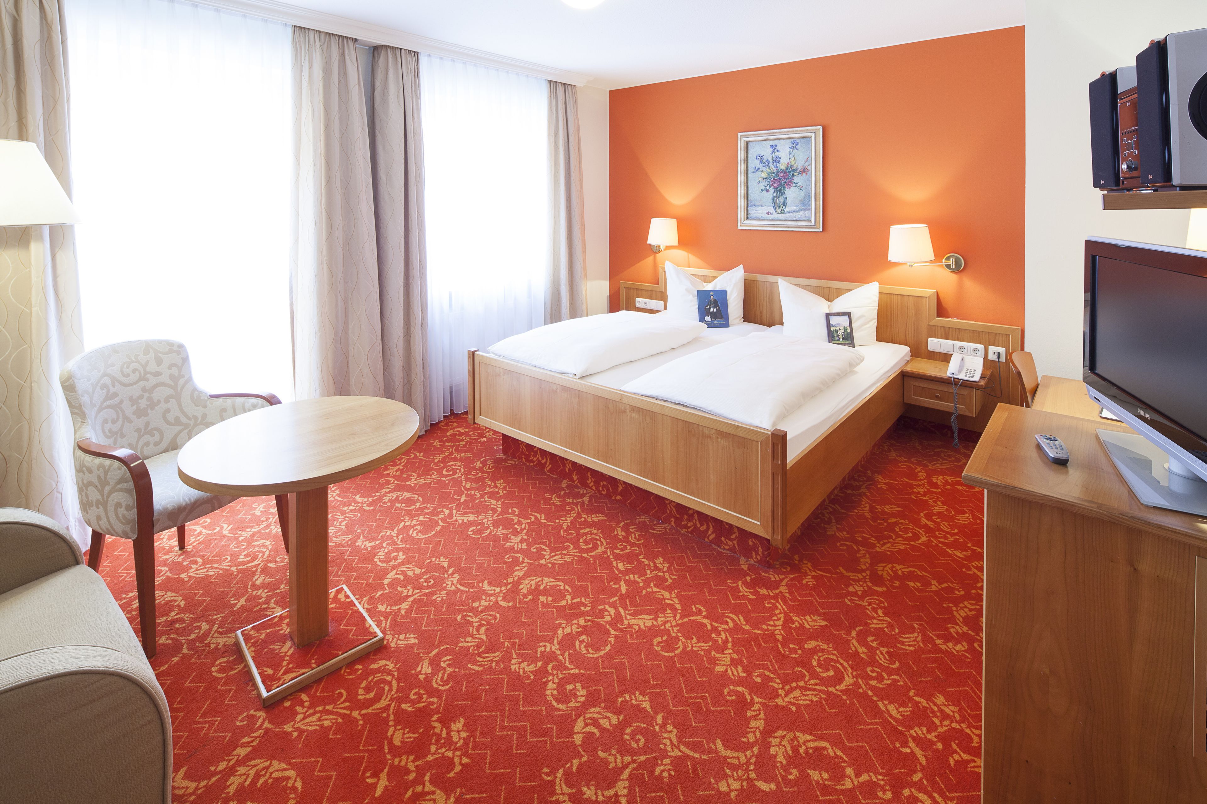 Ein Hotelzimmer mit einem Bett, zwei Nachttischen, einem Fernseher, einem Sessel und einem Schreibtisch.