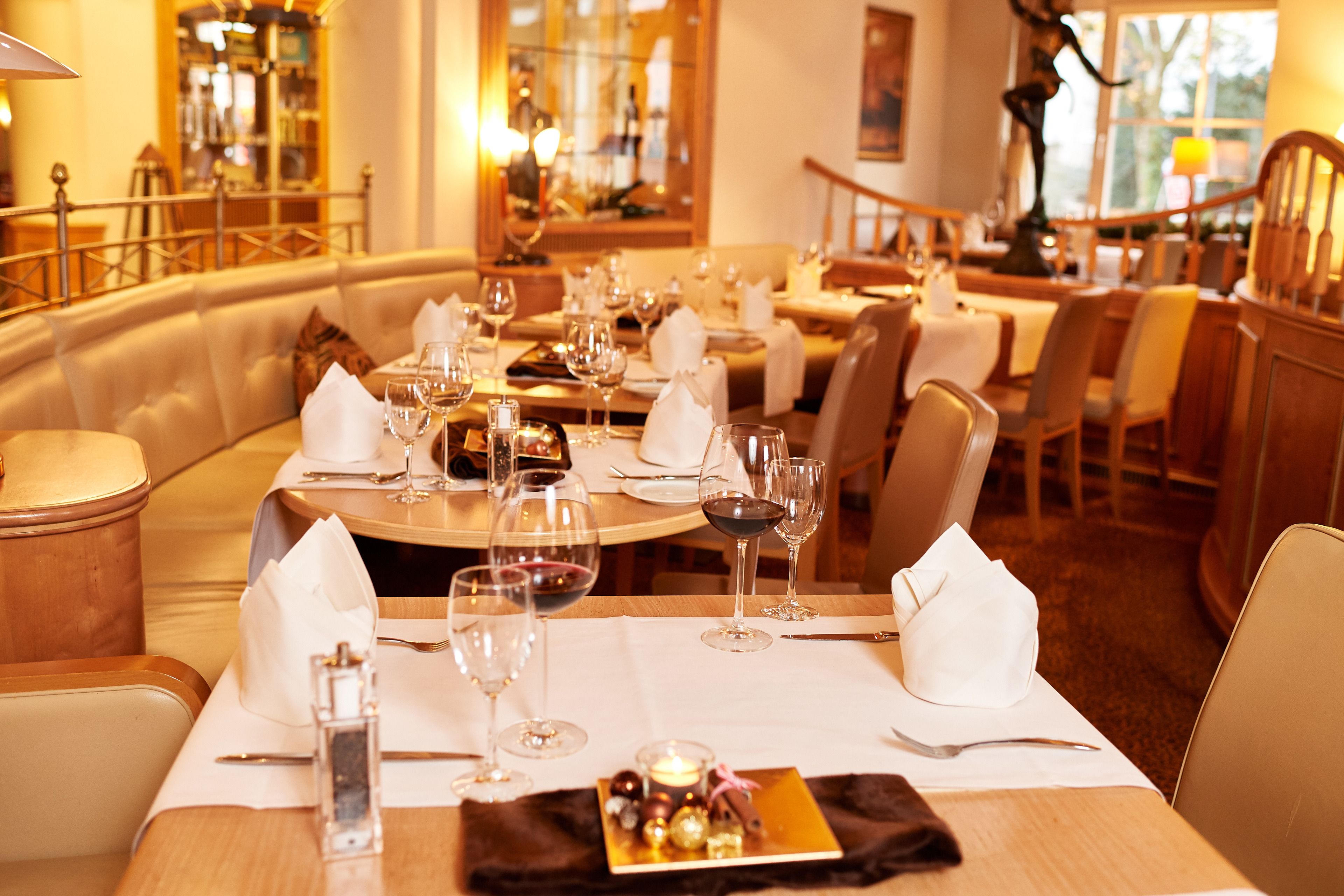 A restaurant with round tables set for dining, each with a white tablecloth, wine glasses, and a candle centerpiece.