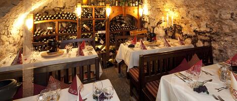Un comedor subterráneo con mesas dispuestas para una comida, rodeado de bodegas y botellas de vino.