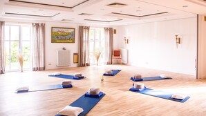 A spacious room with wooden flooring, large windows with curtains, and yoga mats arranged for group exercise. - BE BIO Hotel be active (Toenning)
