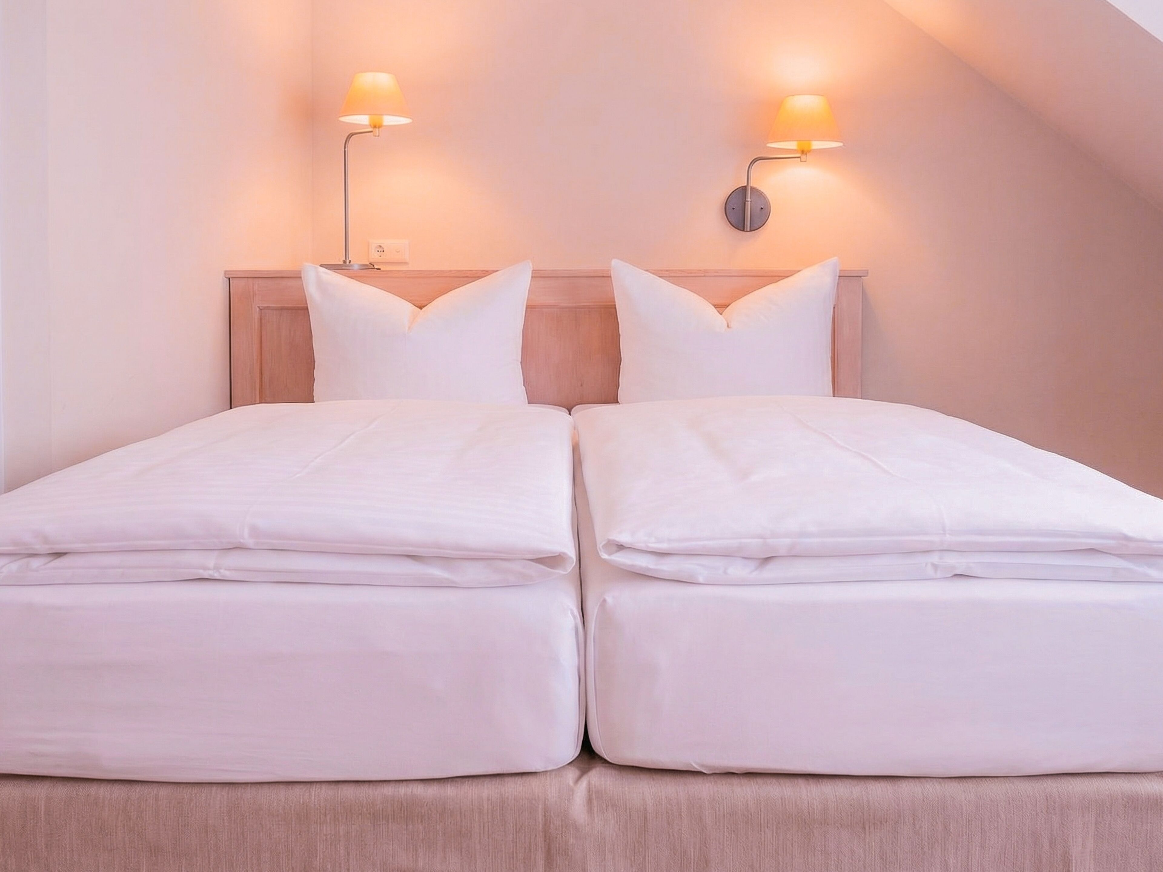 A double bed with two pillows and a wooden headboard. There are two wall-mounted lamps on either side of the bed.