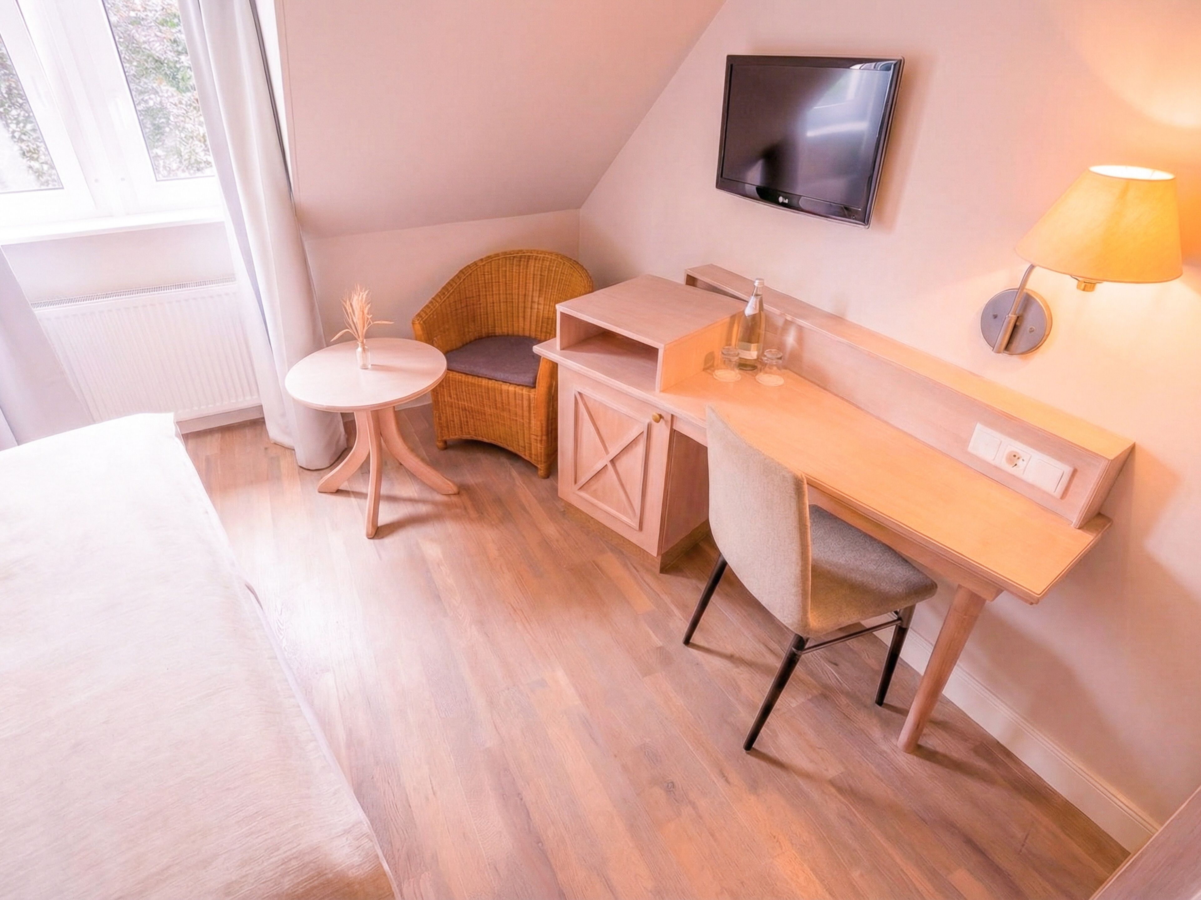 A modern hotel room with a bed, a desk, a chair, a television, and a lamp.