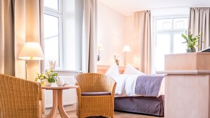 A hotel room with a bed, two wicker chairs, a small table with a lamp, and a view of the street. - BE BIO Hotel be active (Toenning)