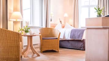 Habitación de hotel con cama, dos sillones de mimbre, una mesita con lámpara y vista a la calle.
