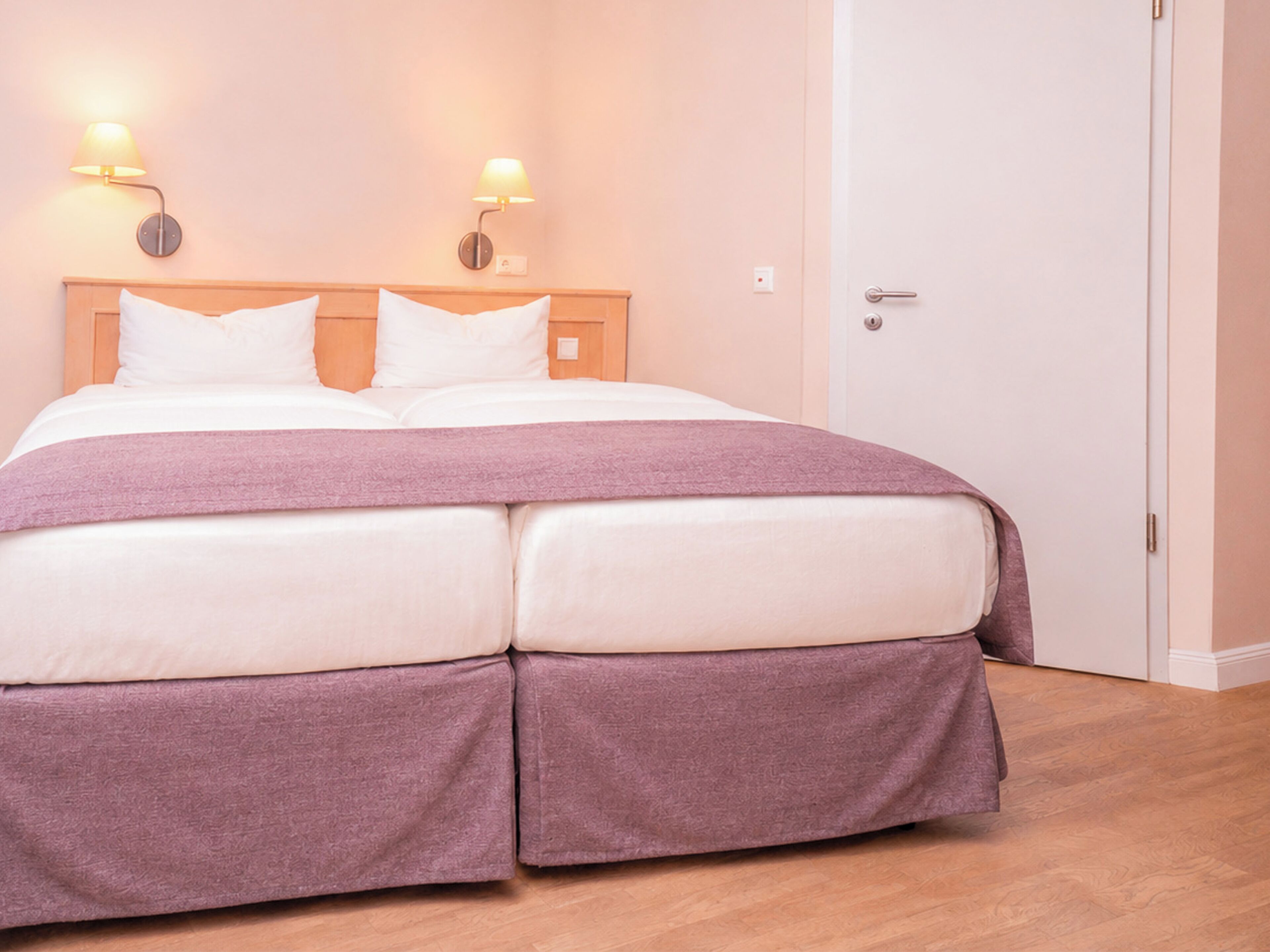A double bed with a headboard, two wall-mounted lamps, and a door to the right.