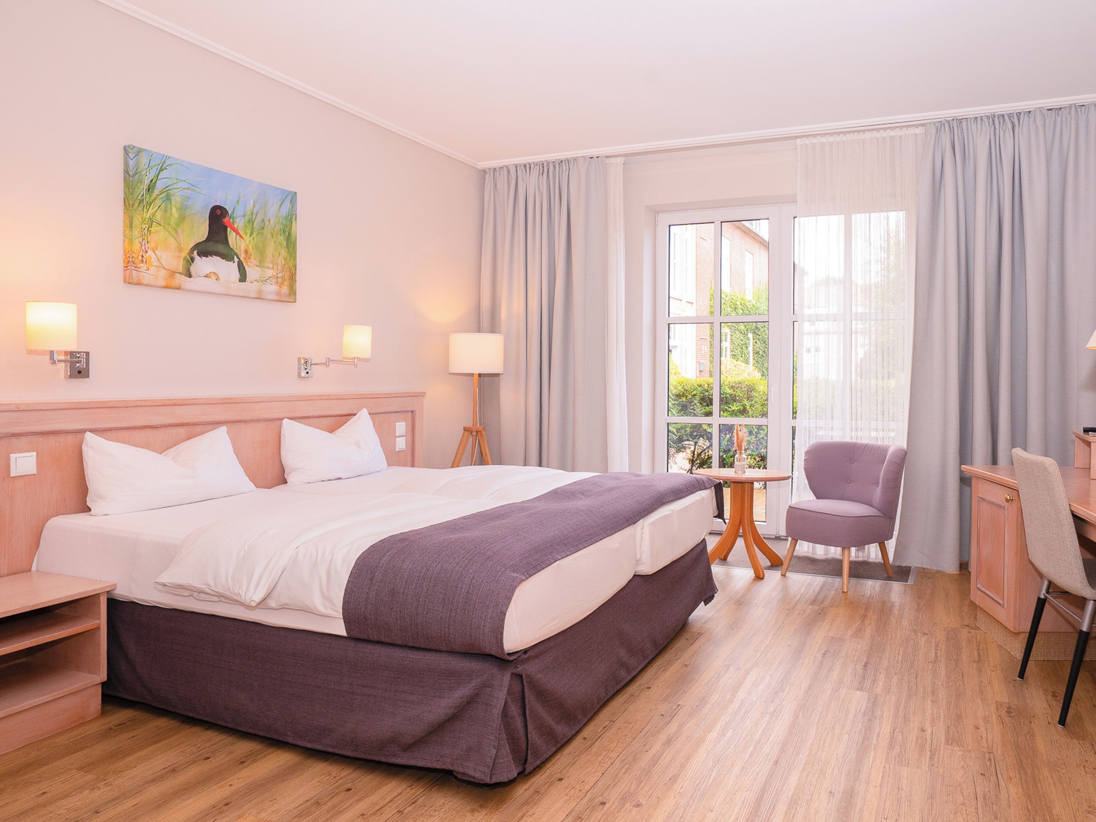 A hotel room with a large bed, bedside lamps, a desk, a chair, and a window with curtains.