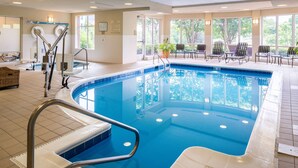 An indoor swimming pool with clear water, a lifeguard chair, and a sunlit area with chairs and a potted plant. - Hilton Garden Inn Charlottesville (Charlottesville)