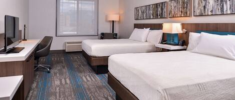 A hotel room with two beds, a desk with a computer, a chair, a lamp, and artwork on the wall.