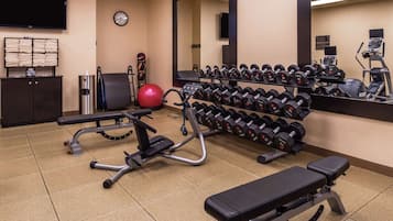 Una palestra con attrezzature per esercizi, una panca, uno specchio e un orologio a parete.