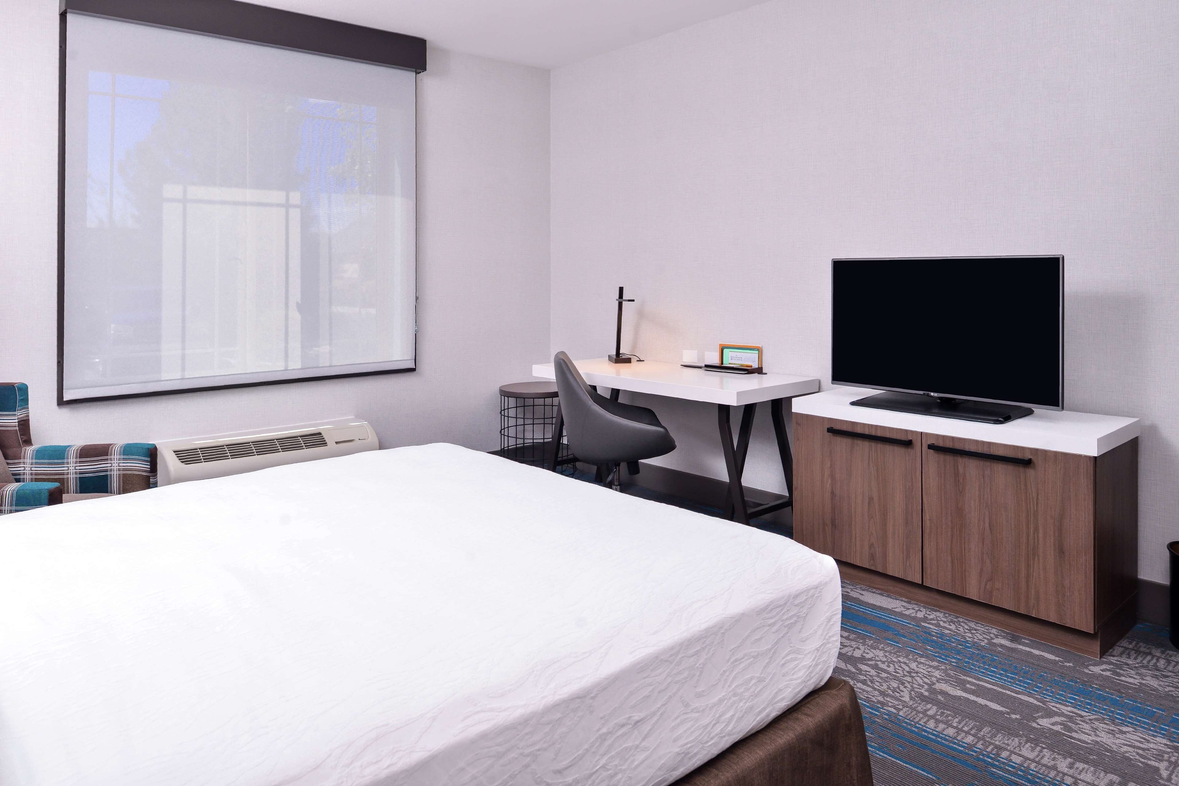 A hotel room with a bed, a desk with a chair, a television on a cabinet, and a projector screen.