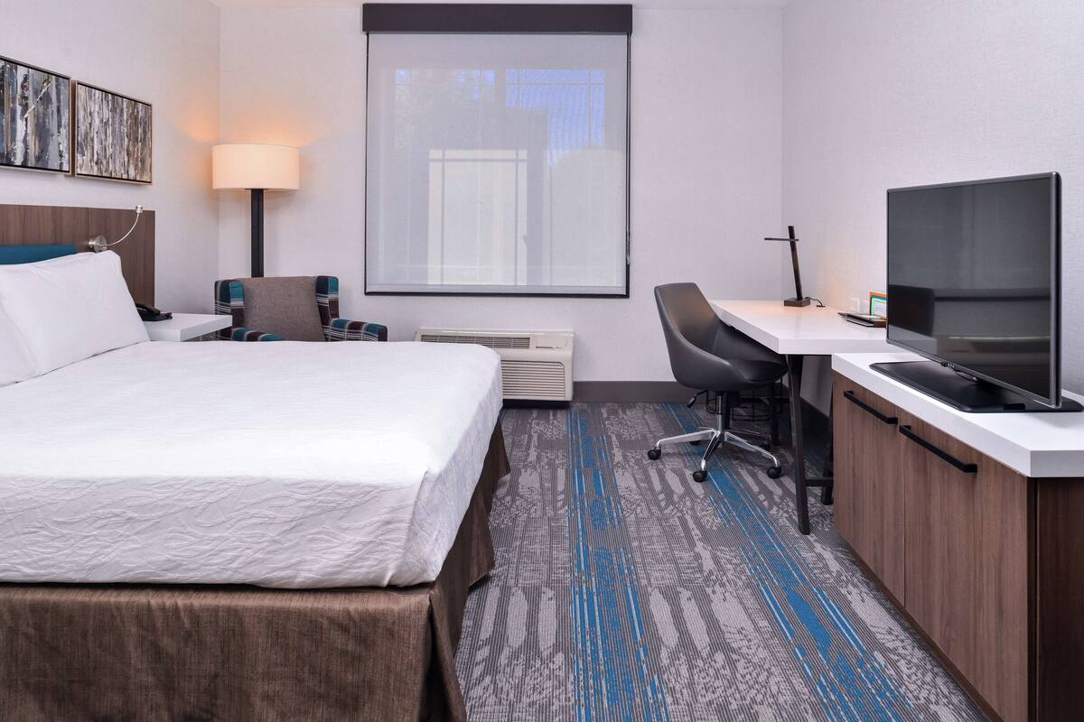 Ein Hotelzimmer mit Bett, Schreibtisch, Fernseher und Fenster.