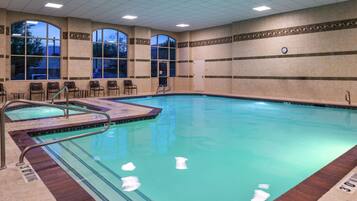 Une piscine intérieure à l’eau claire, avec un escalier et quelques chaises disposées près du bord.