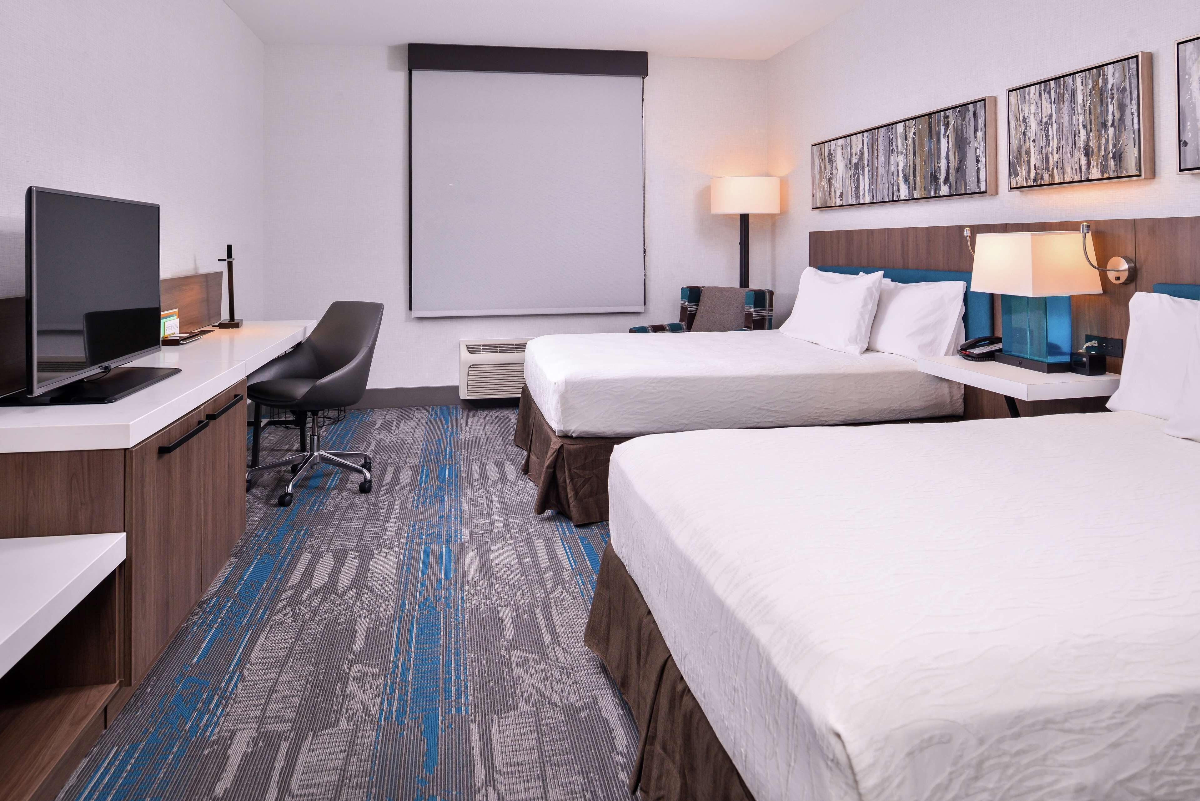 A hotel room with a desk, two beds, a TV, and artwork on the wall.