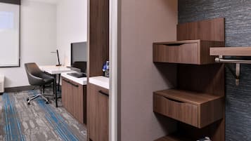 A modern office space with a desk, chair, and computer. There is a water bottle on the desk and a small shelf with a cup. The room has a carpeted floor and a window.