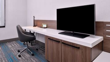 A modern office desk with a flat-screen monitor, a black chair, and a small table with a device.