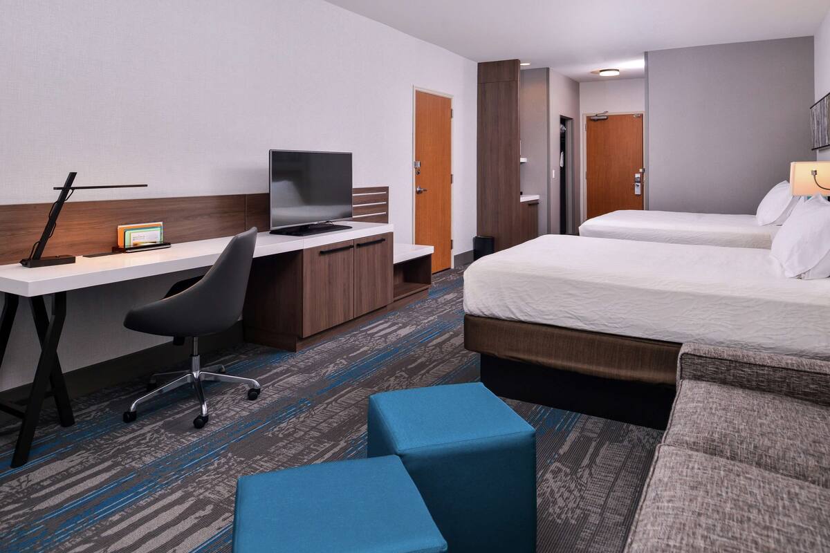 Ein Hotelzimmer mit Schreibtisch, Computer, Stuhl, zwei Betten und einer kleinen Sitzecke.