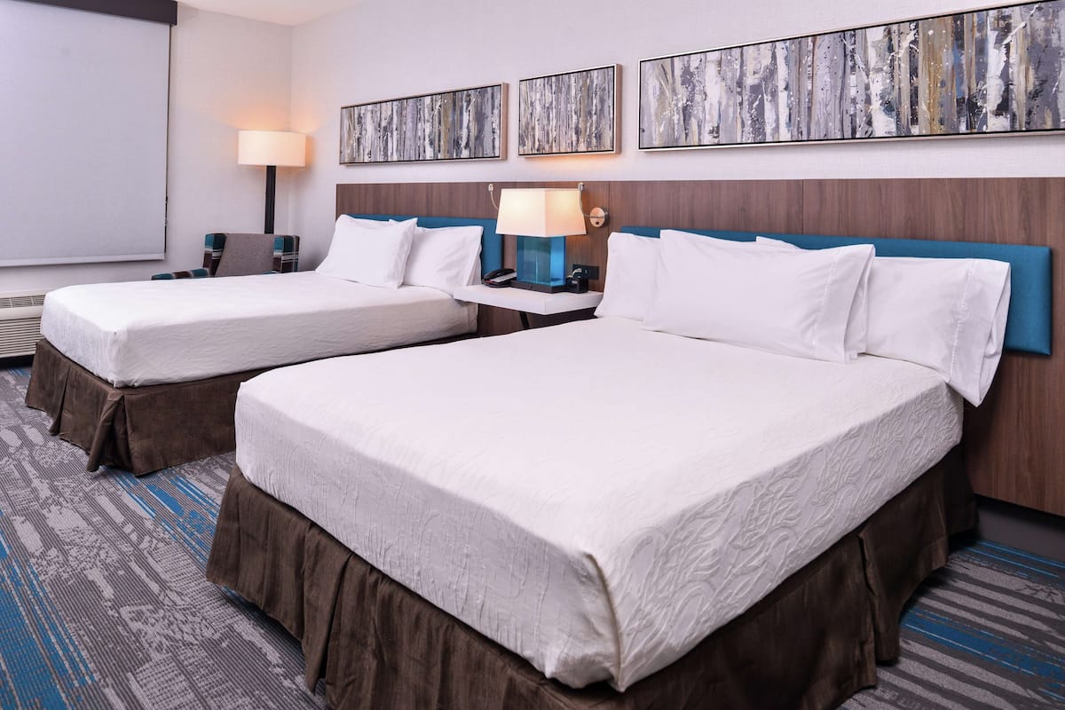 Ein Hotelzimmer mit zwei Betten, einem Nachttisch mit Lampe und einem großen abstrakten Gemälde an der Wand.