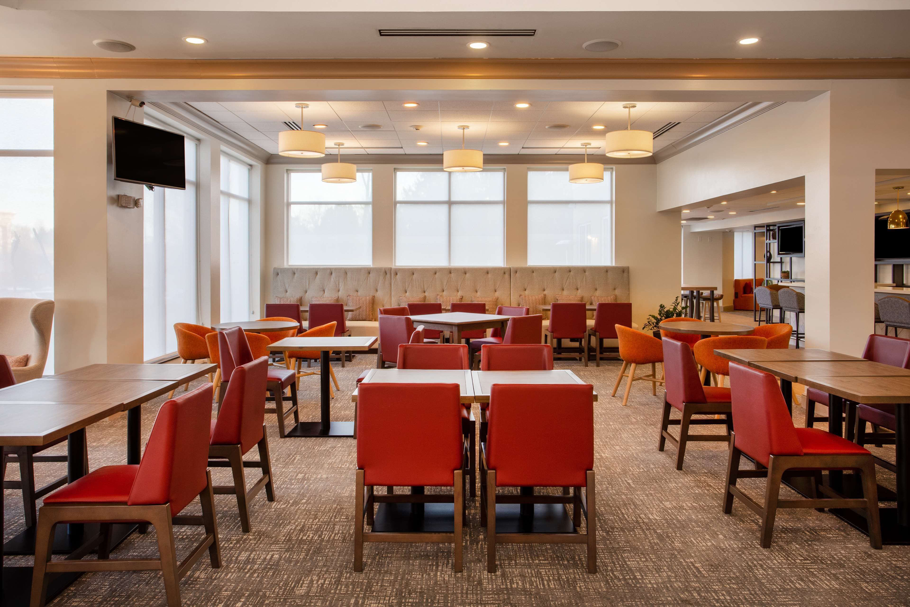Un vaste espace dédié à la salle à manger, avec de nombreuses tables et chaises, de grandes fenêtres et des luminaires au plafond.