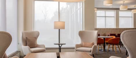 Un moderno vestíbulo de hotel con asientos cómodos, una mesa redonda y un ventanal con vistas al exterior.